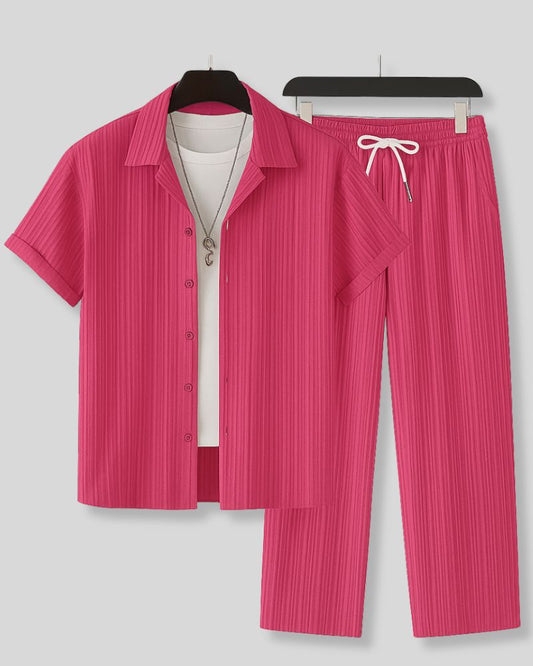 Pink pleated shirt and pants set on hangers against a gray background